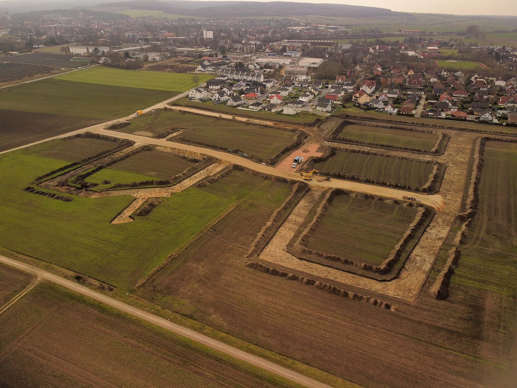 Luftaufnahme des Baugebiets Ziegenberg mit freien Grundstücken, Erschließungsstraßen und angrenzender Wohnbebauung in grüner Umgebung.